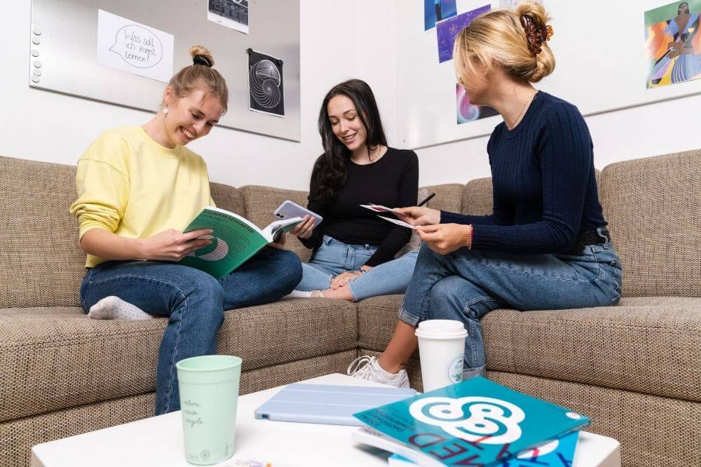 Drei Freundinnen sitzen zusammen auf dem Sofa und lernen gemeinsam für den MedAT. | Studienorte Österreich